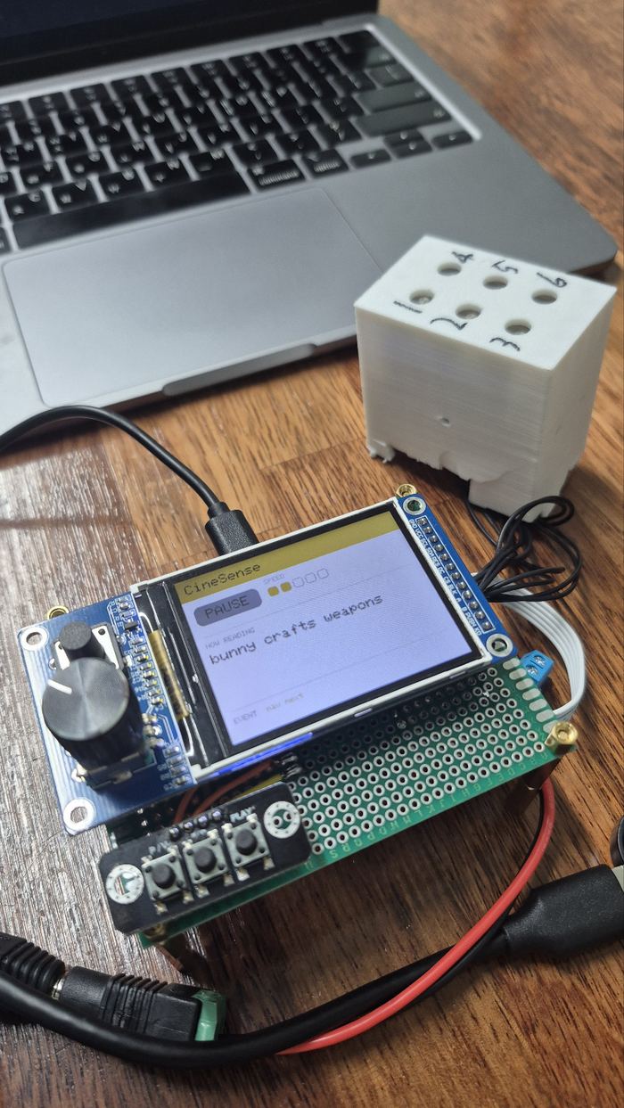 Prototype with a status screen, dial and buttons, beside a white 3D-printed braille cell
