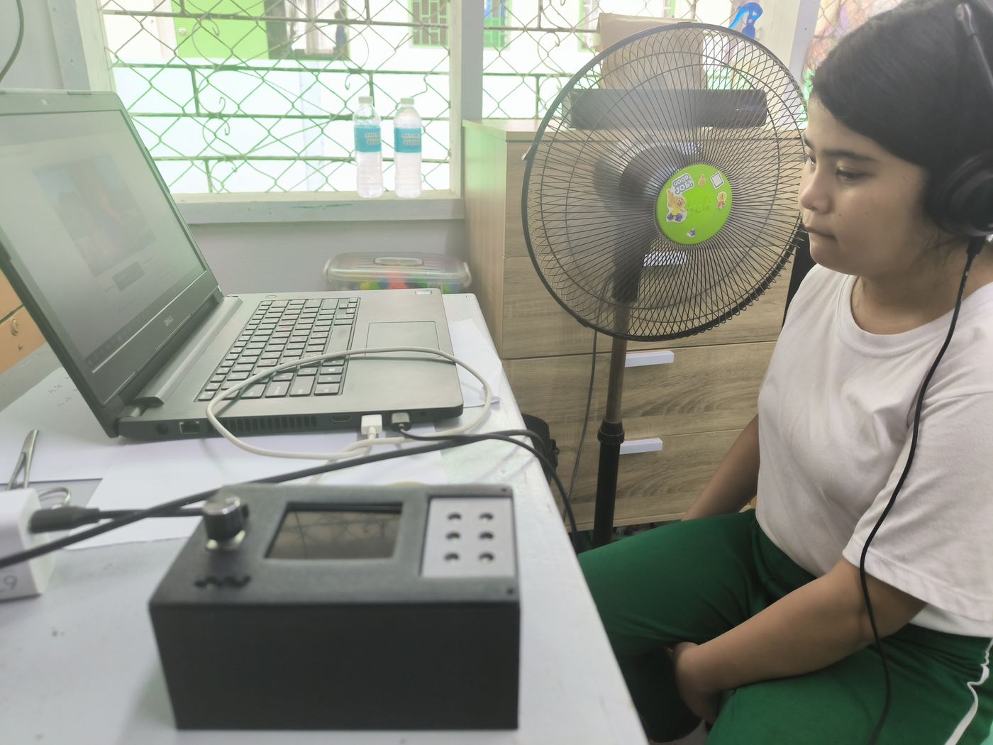 A student wearing headphones listens to a video on a laptop, with the CineSense braille device on the desk.