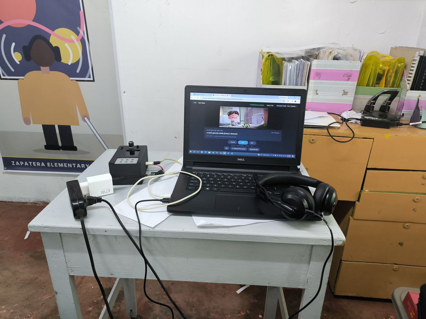 A classroom desk set up with a laptop, headphones and the CineSense device.
