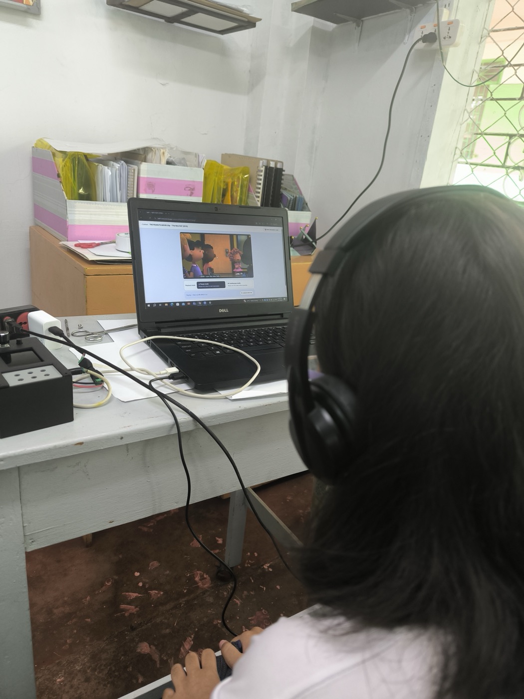A student with headphones faces a laptop playing a described video.